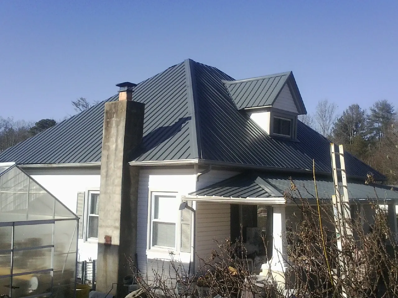 Dark blue standing seam metal roof on a white farmhouse with dormer — Slate & Tile Roof Repair by Roofing Brothers in Collierville