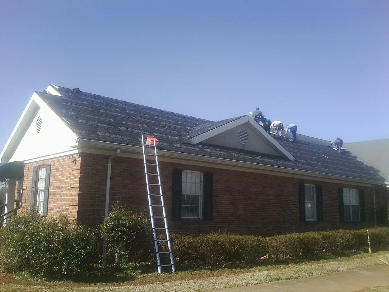 Crew tearing shingles off a brick ranch roof with a ladder set — Metal Roof Repair work by our crew in Collierville