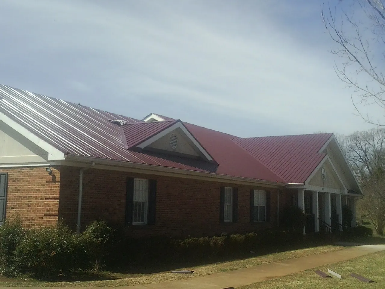 Red metal roof with gabled entries on a long brick building, from a Hail Damage Roof Repair job in Collierville